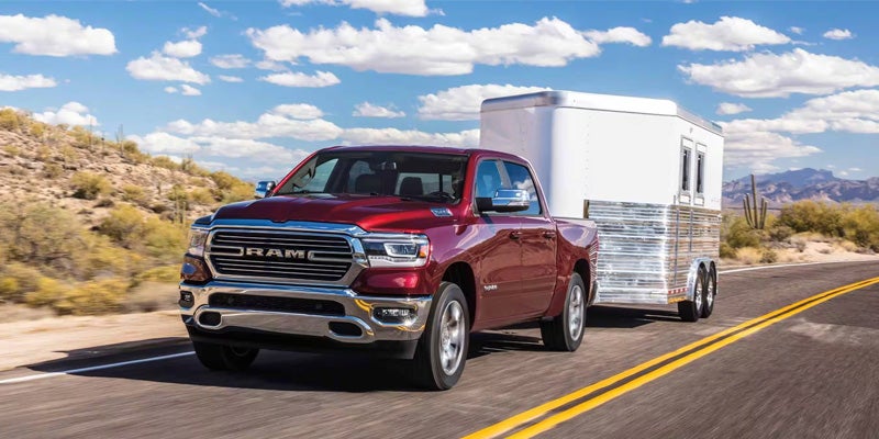 An image of a red 2024 RAM 1500 full-size pickup truck pulling a trailer down the highway