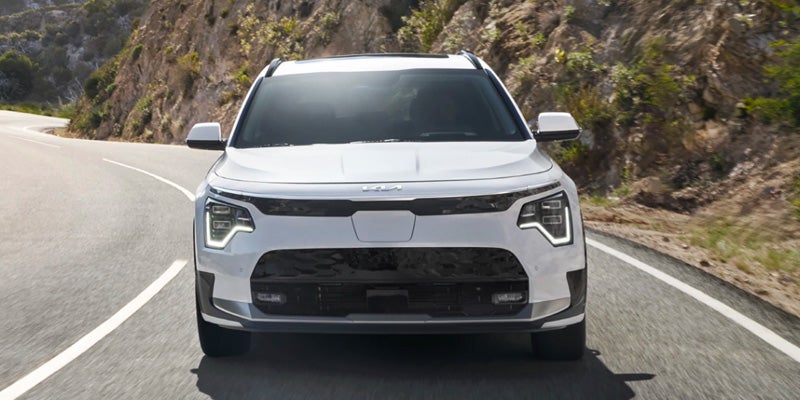 A head-on image of a white Kia Niro EV driving straight towards the camera along a winding highwy