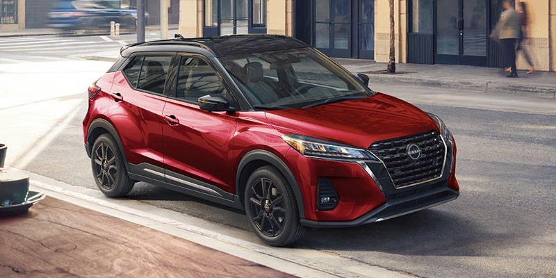 An image of a dark red metallic 2024 Nissan Kicks sitting on a city street corner. 
