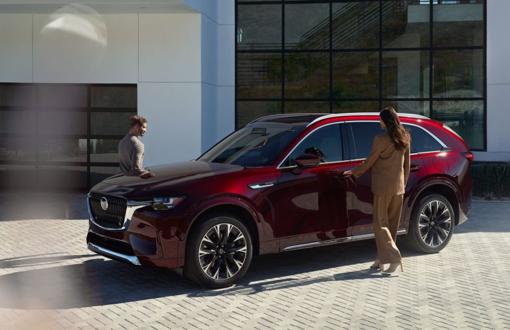 A red CX-90 in front of the showroom, with a woman about to get into the driver's seat